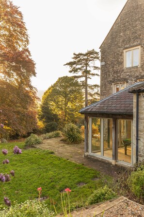 A stone house with a glass conservatory, surrounded by a well-maintained garden with various plants and flowers. - Georgian House With Garden Views Tennis Court (Bath)