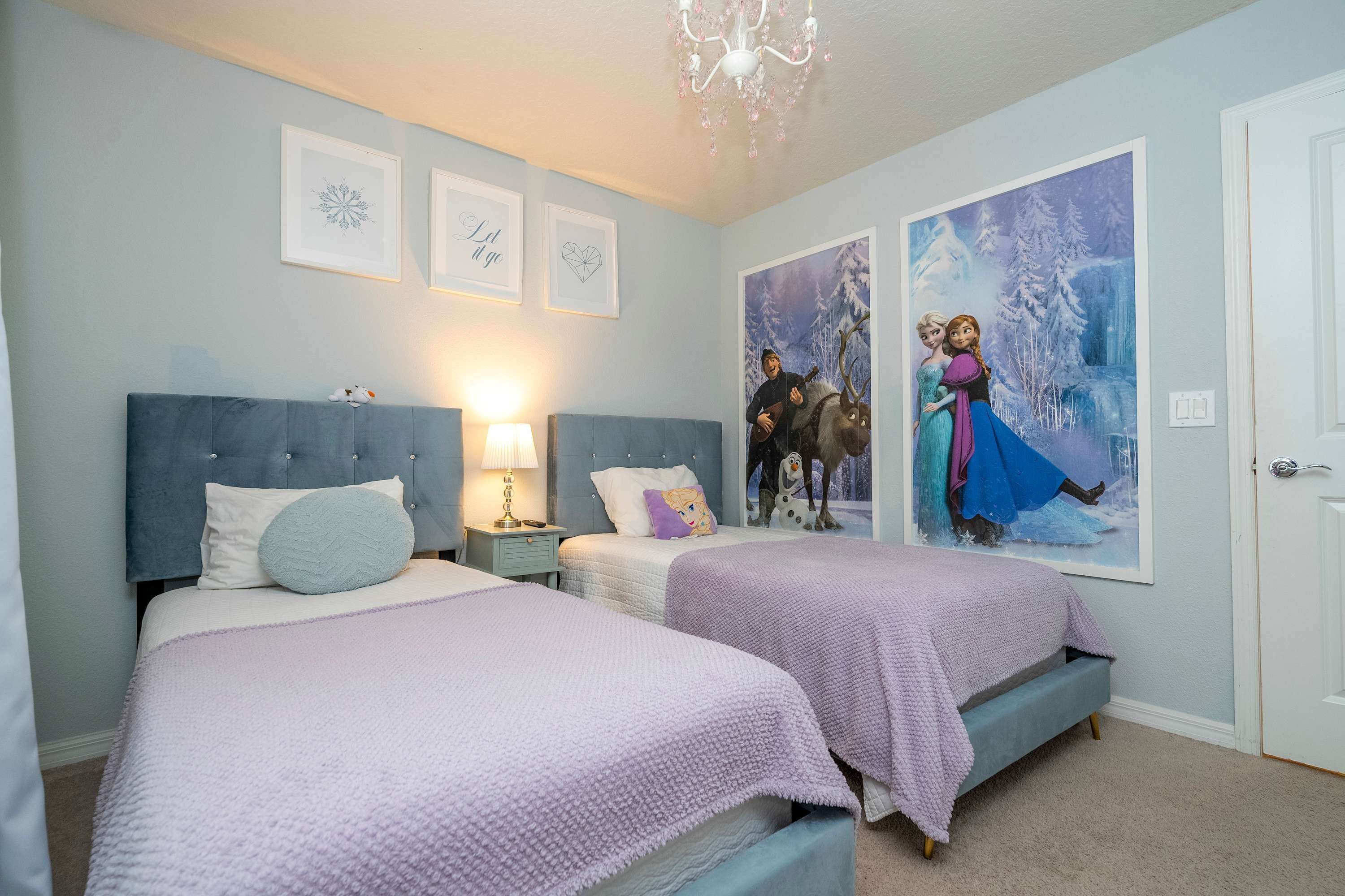 A bedroom with two beds, a chandelier, and wall art.
