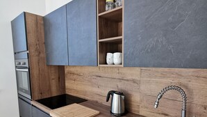 A modern kitchen with dark cabinets, a wooden countertop, a stainless steel sink, and a built-in shelf with jars. - Apartments Egis Koper (Koper)