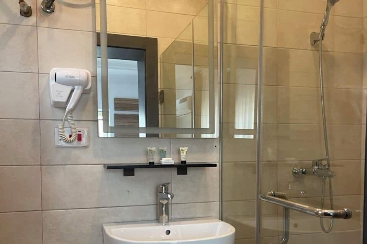 Ein Badezimmer mit einem weißen Waschbecken, einem Spiegel, einer Handbrause und einem an der Wand befestigten Föhn.