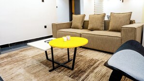 Ein modernes Wohnzimmer mit einem beigen Sofa, einem gelben Tisch und einem grauen Sessel.