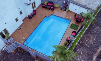An outdoor swimming pool with a wooden deck, surrounded by outdoor furniture and potted plants.
