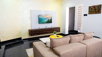 Una sala de estar moderna con un sofá color beige, una mesa de centro amarilla, un televisor de pantalla plana montado en la pared y un aparador de madera con objetos decorativos.