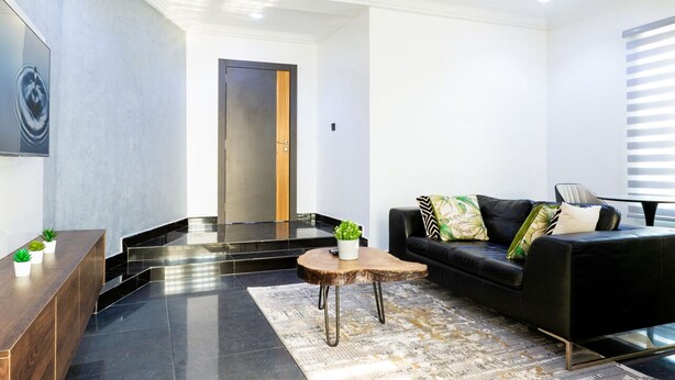 Ein modernes Wohnzimmer mit einer schwarzen Ledersofa, einem Holztisch und einem schwarzen Ledersessel. An der Wand hängt ein großes Gemälde und auf dem Tisch steht eine kleine Pflanze.