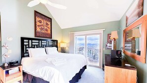 A hotel room with a bed, a nightstand, a desk, a mirror, a ceiling fan, and a balcony with a view.