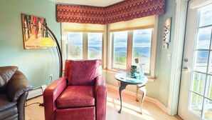 A corner room with a red leather chair, a small round table, and a view of the outdoors through large windows.
