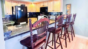 A kitchen with wooden cabinets, a black refrigerator, a microwave, and a granite countertop.