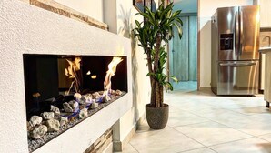 A modern kitchen with a built-in fireplace, a potted plant, and a stainless steel refrigerator.