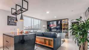 A modern living space with a central island, a flat-screen TV, and a large window offering a city view.