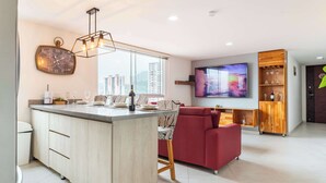 A modern kitchen with a central island, a red sofa, and a TV in the living area.
