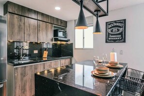 Une cuisine moderne avec des meubles en bois foncé, un plan de travail noir et un îlot central. On y trouve un four à micro-ondes, un évier et un luminaire suspendu au-dessus de l’îlot.