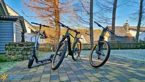 A paved driveway with two bicycles parked on it, a stone wall, and a wooden fence in the background.