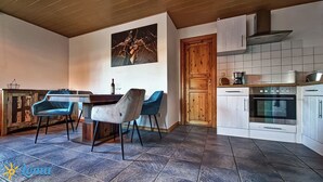 A kitchen with a dining area, featuring a wooden door, white cabinets, and a tiled floor.