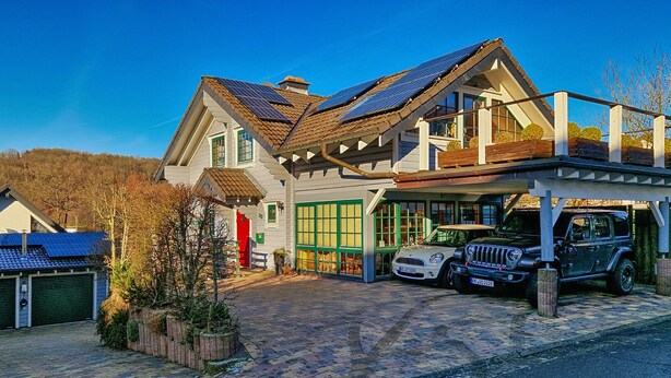 A two-story house with a garage, solar panels on the roof, and two cars parked in the driveway.