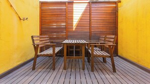 Une table et des chaises en bois sont placées devant un mur jaune, et une clôture en bois se trouve à l’arrière-plan.
