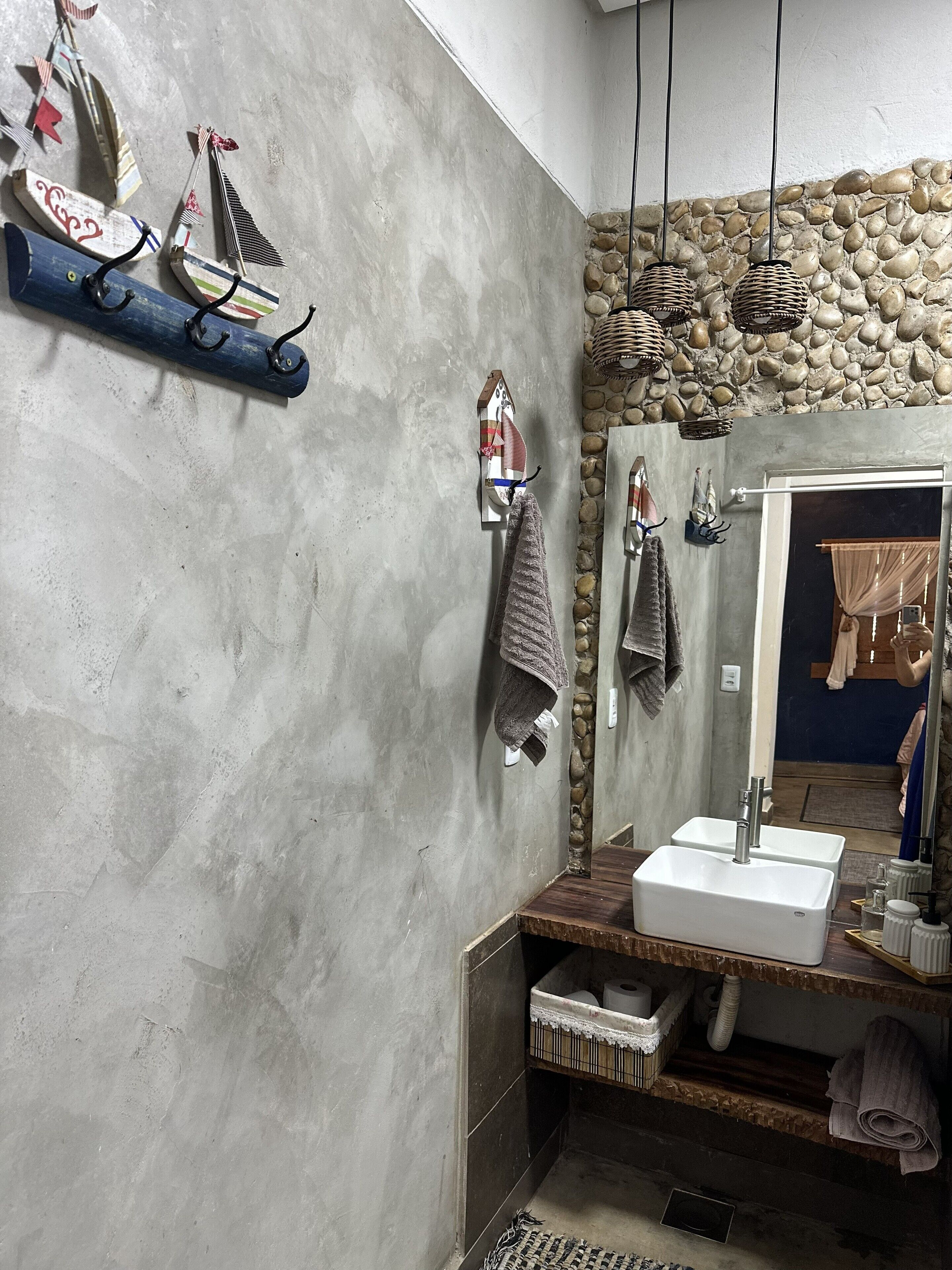 A bathroom with a stone wall, a wooden vanity, a large mirror, and a hanging light fixture.