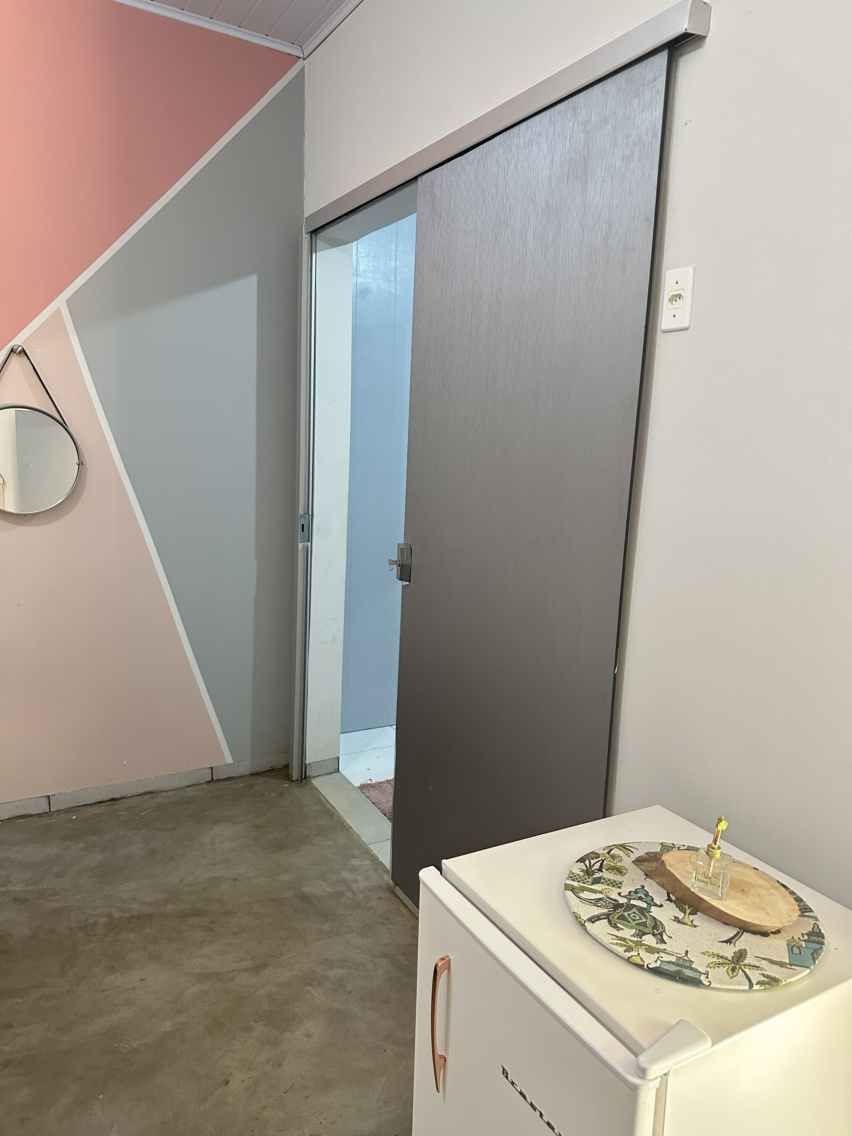 Una habitación con puerta corrediza, un refrigerador pequeño y un espejo instalado en la pared.