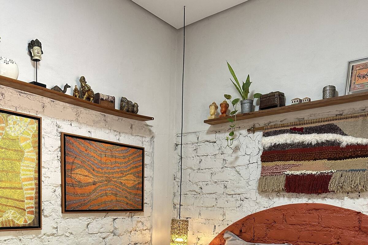 A modern bedroom with a brick wall, a bed with grey bedding, a headboard, and decorative items on shelves.