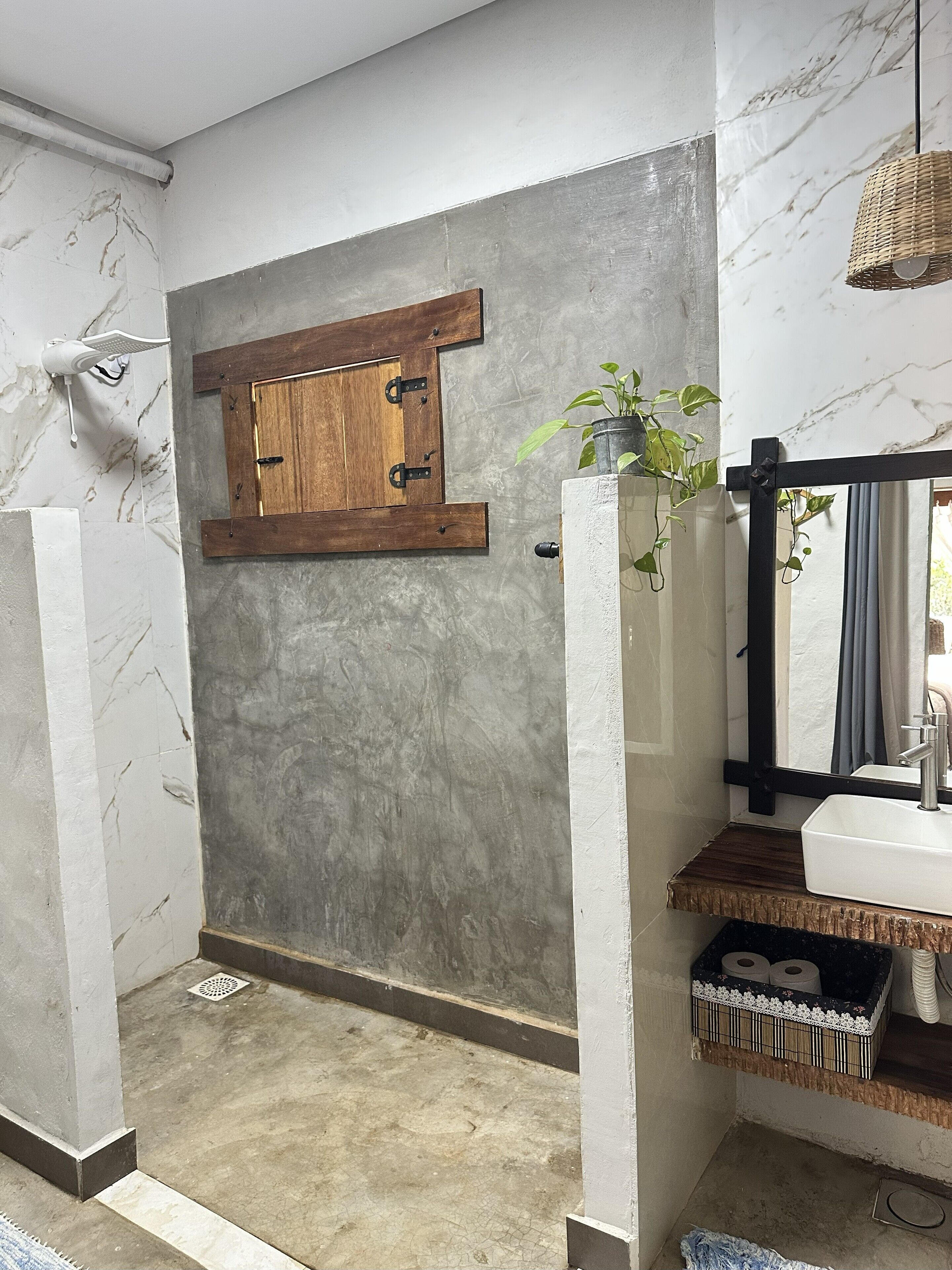 Un bagno con parete in marmo, porta in legno, lavabo con specchio e una pianta pensile.