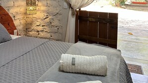 Una camera da letto con un letto, una testata in legno, una parete bianca, una lampada a sospensione e vista sul verde.