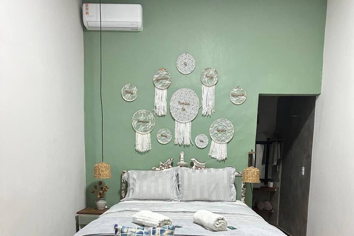 A bedroom with a bed, bedside tables, a wall-mounted air conditioner, and a door leading to another room.