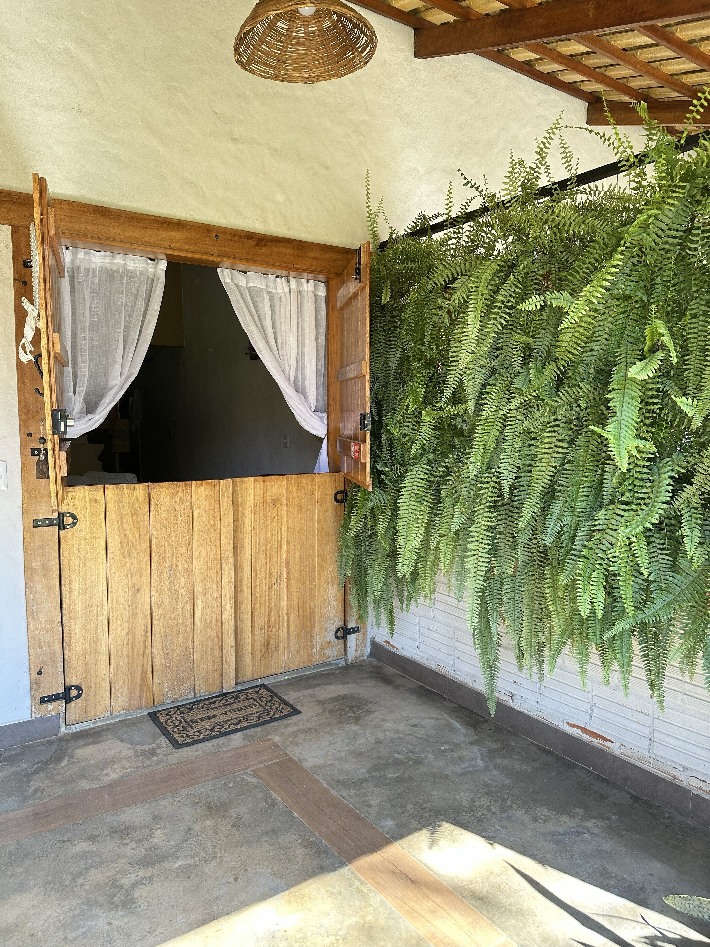 Una puerta de madera con dos cortinas, un suelo de hormigón y una pared con helechos colgantes.