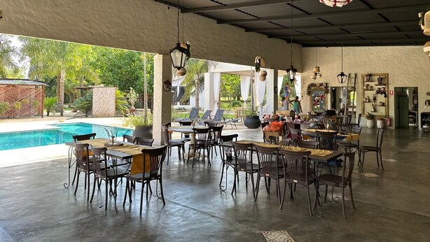 Un'area pranzo interna con tavoli e sedie, una piscina e luci decorative appese.