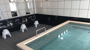 A swimming pool with a tiled floor and a wooden edge. There are white stools and a mirror above the pool. - Hotel Alpha-One Yamaguchi Inter (Yamaguchi)