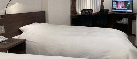 Quarto de hotel com duas camas, uma escrivaninha com computador e uma cadeira.