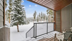 A wooden deck with a metal railing, a bench, and snow-covered trees in the background. - Atrium 005: Historic District Ski Condo, Fireplace, Hot Tub Access. (Breckenridge)