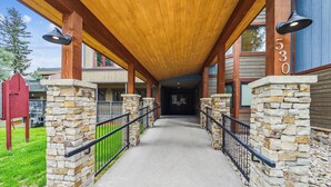 A covered walkway with stone pillars and a wooden ceiling, leading to a building entrance. - Atrium 005: Historic District Ski Condo, Fireplace, Hot Tub Access. (Breckenridge)