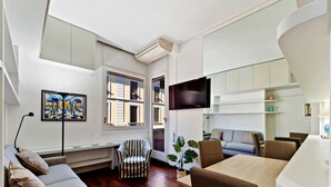 Una sala moderna con sofá, sillón, mesa de comedor y televisor montado en la pared.