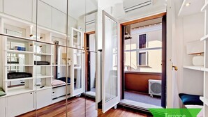 Una habitación moderna con suelo de madera, muebles blancos y un ventanal de vidrio que da a una terraza.