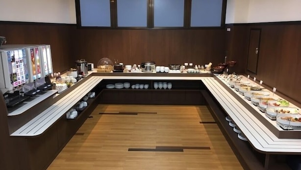 Montaje tipo buffet con varias estaciones de servicio, una máquina de café y una variedad de platos exhibidos en estantes.