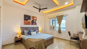 Une chambre à coucher moderne, avec un lit, des tables de chevet, un bureau, une chaise, un ventilateur de plafond et des œuvres d’art accrochées au mur.