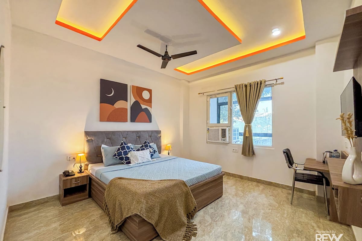 A modern bedroom with a bed, bedside tables, a desk, a chair, a ceiling fan, and artwork on the wall.