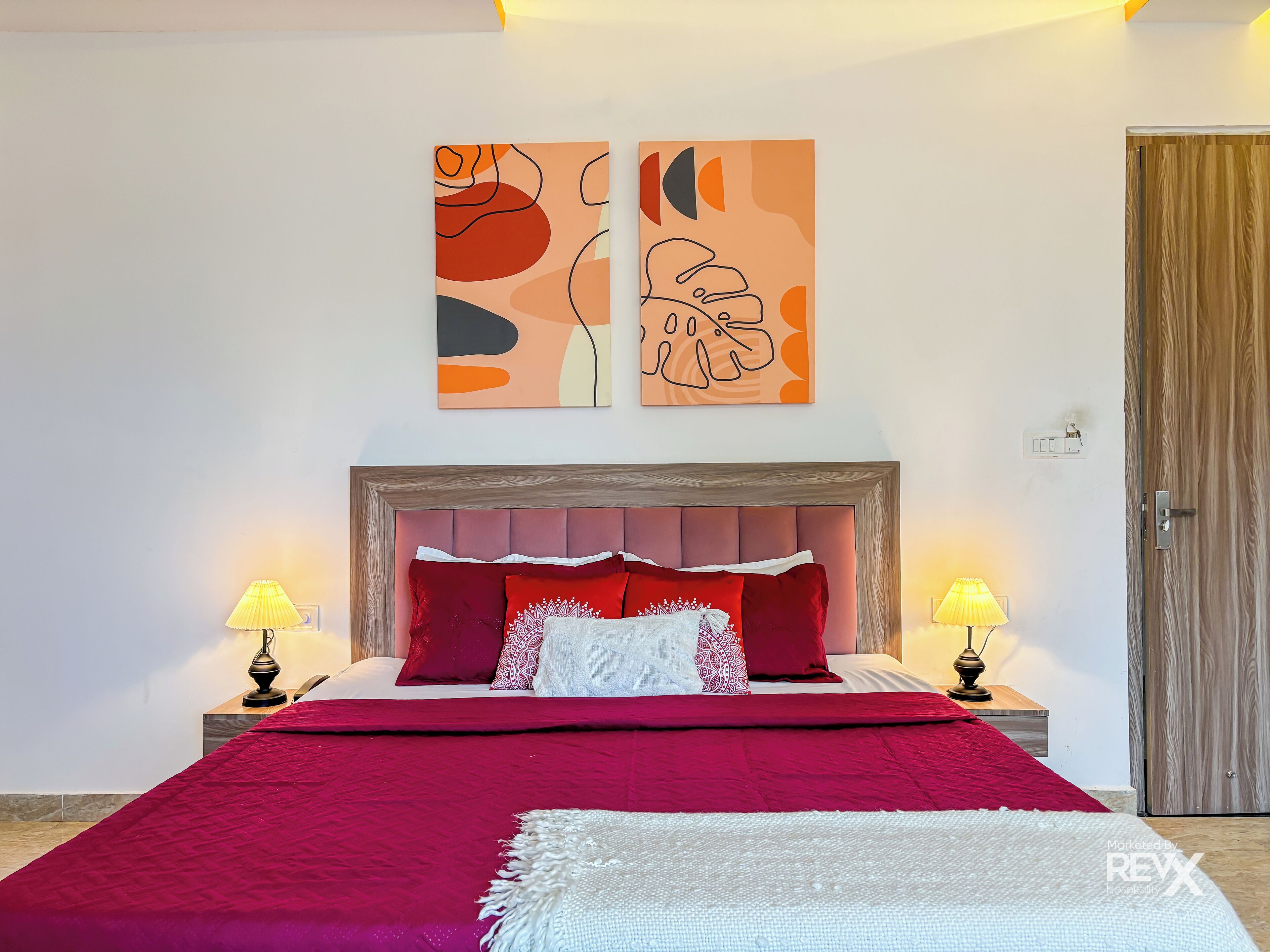 Een slaapkamer met een groot bed, twee bedlampen en abstracte kunst aan de muur.