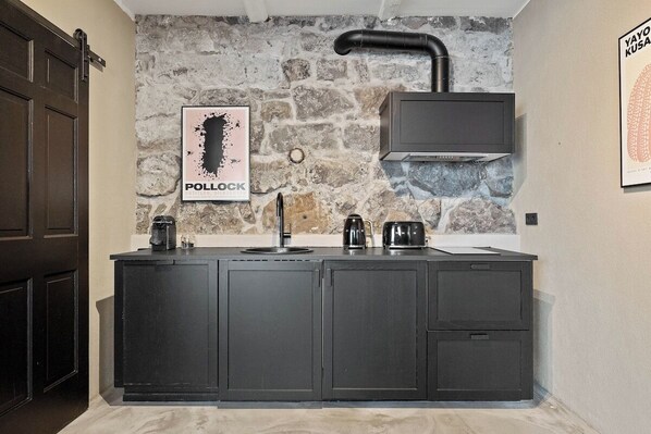 Una cocina con pared de piedra, una cafetera, un hervidor y un cartel enmarcado en la pared.