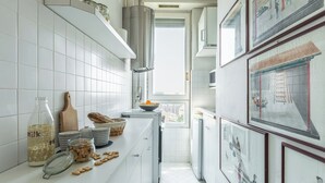 Una cocina estrecha con azulejos blancos, una campana extractora de acero inoxidable y una ventana con vistas a edificios.
