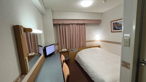 Una habitación de hotel con cama, escritorio, computadora, teléfono y ventana con cortinas.