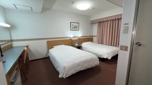 Habitación de hotel con dos camas individuales, un escritorio, una silla, una mesita de noche con teléfono y un cuadro en la pared.