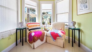 Habitación de esquina con dos sillones, una mesita y ventana con vista a una casa.