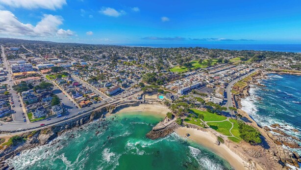 Vista aérea de un pueblo costero con playa, costa rocosa y una combinación de edificios residenciales y comerciales.