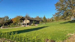 Ein rustikales Blockhaus mit geneigtem Dach, umgeben von einem gepflegten Rasen und Bäumen.
