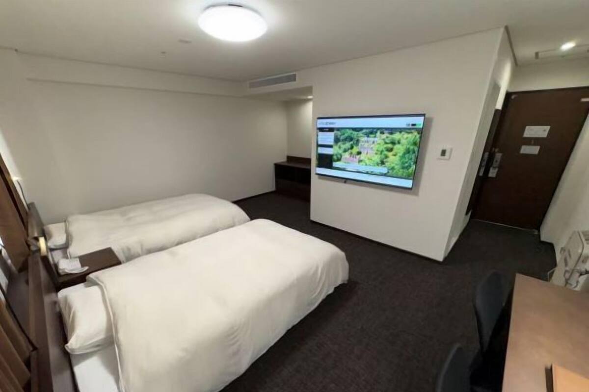 A hotel room with two single beds, a flat-screen TV mounted on the wall, and a desk with a chair.