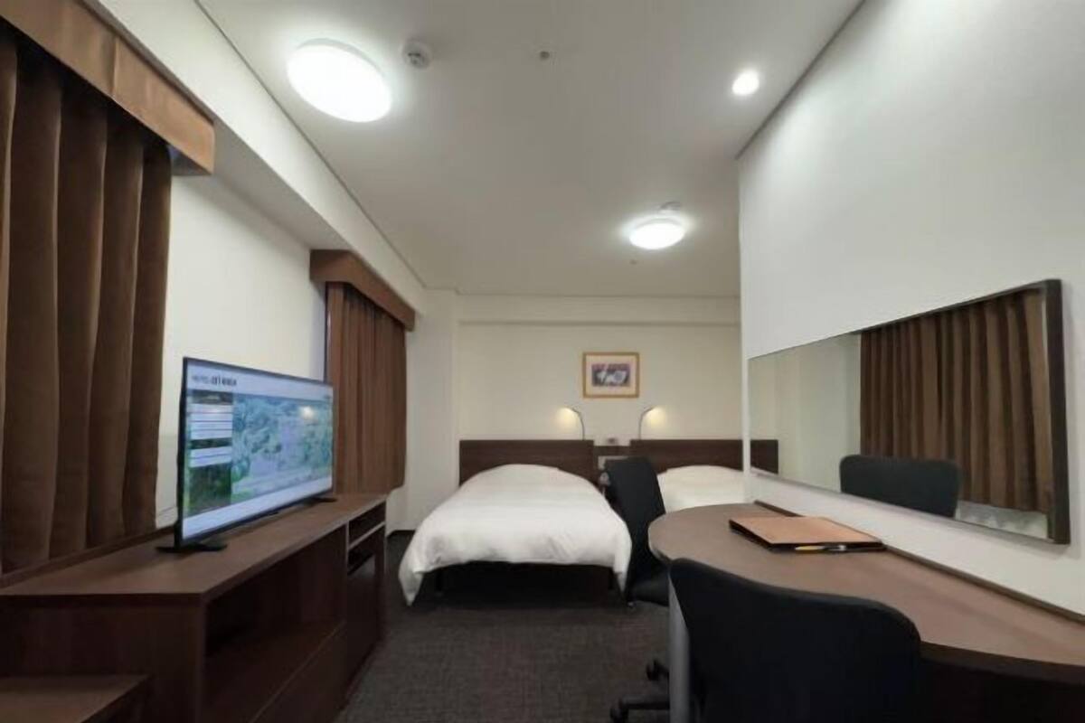 A hotel room with a bed, a desk, a chair, a television, and a mirror.