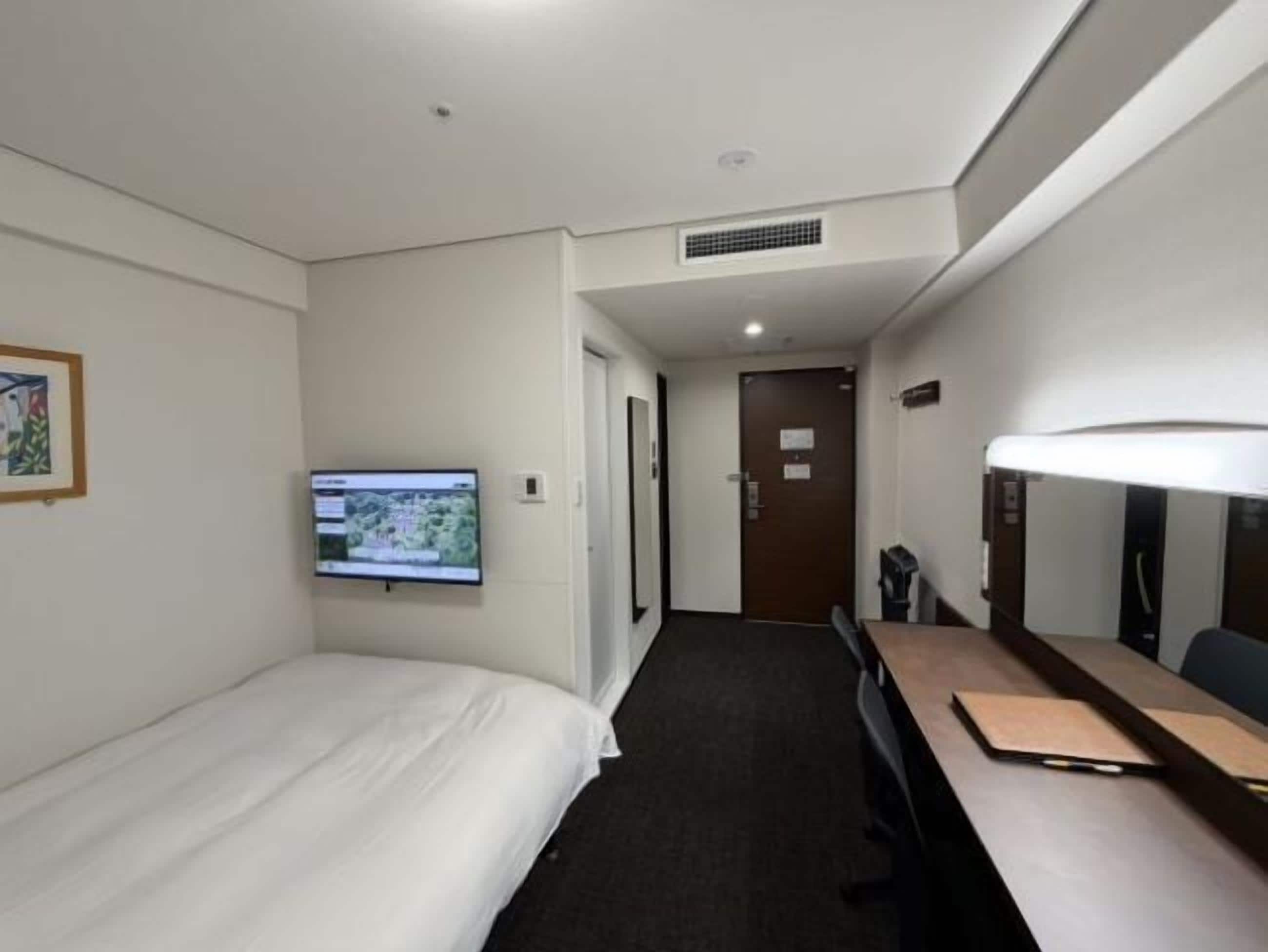 A hotel room with a bed, a desk, a television, and a door leading to another room.