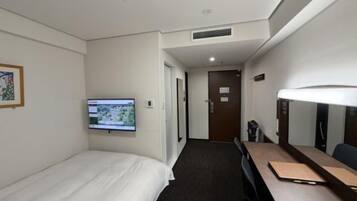 A hotel room with a bed, a desk, a television, and a door leading to another room.