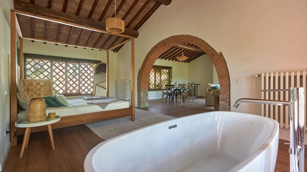 A spacious room with a large white bathtub, wooden flooring, and a dining area with a table and chairs. - Tenuta Pian Del Gallo, Greve in Chianti, Florence and Chianti (Greve in Chianti)