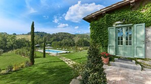 A pool area with a clear view of the surrounding landscape, a stone pathway, and a building with green shutters.